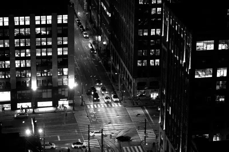Aerial view of a downtown street at night, with office towers, lit windows and traffic moving through an intersection