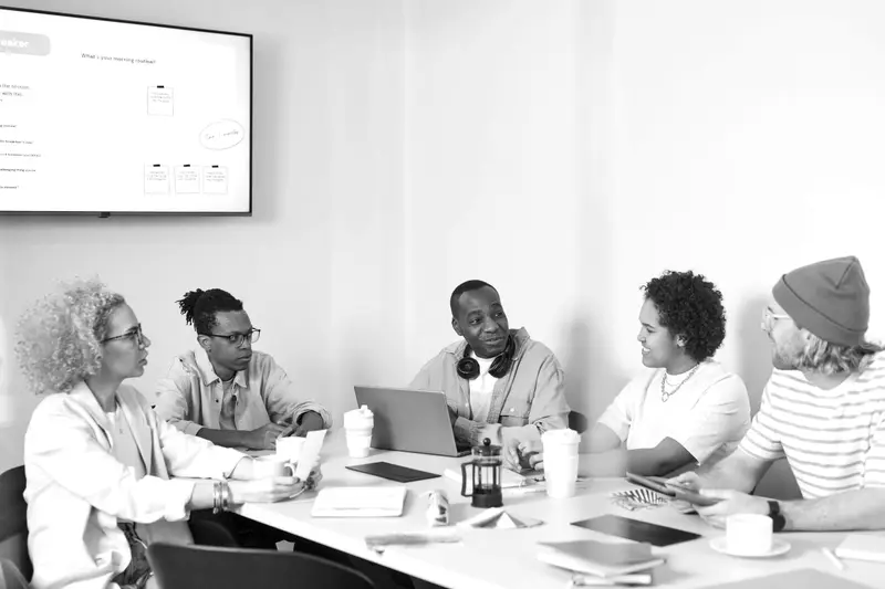 A small team in a meeting room discussing ideas around a table with laptops and notebooks